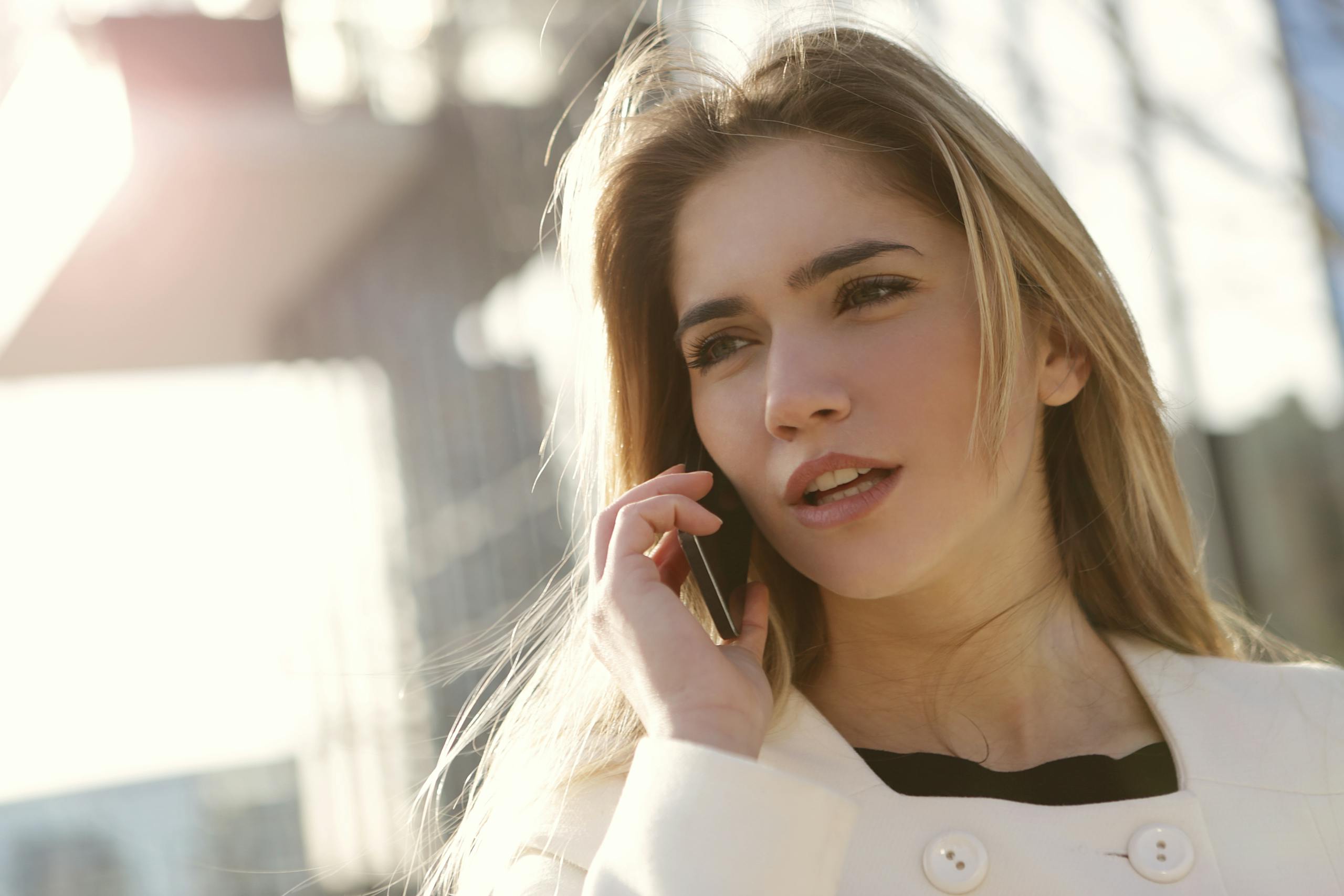 A young woman with blond hair using a smartphone outside on a sunny day.